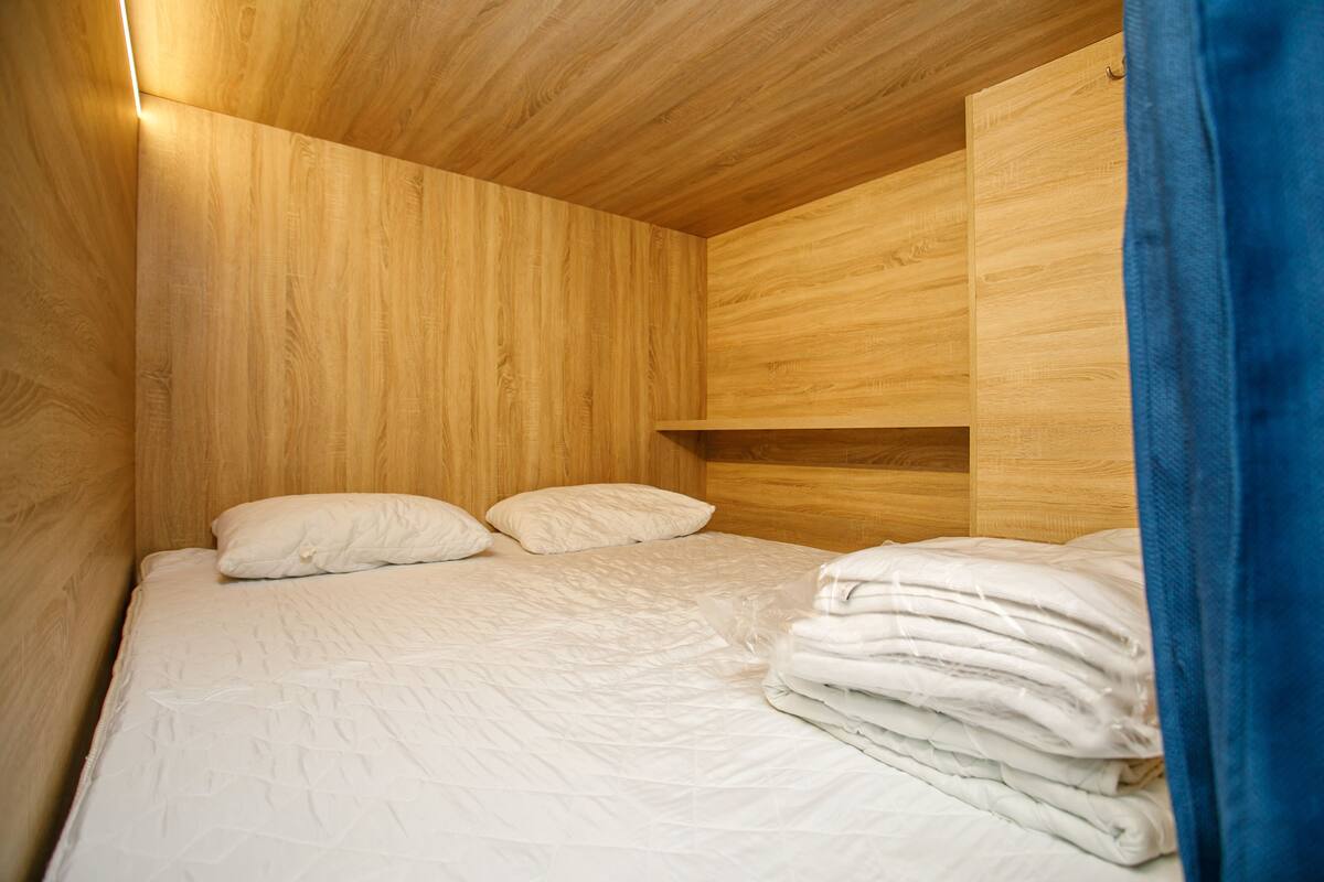A wooden room with a bed, pillows, and a stack of folded blankets.