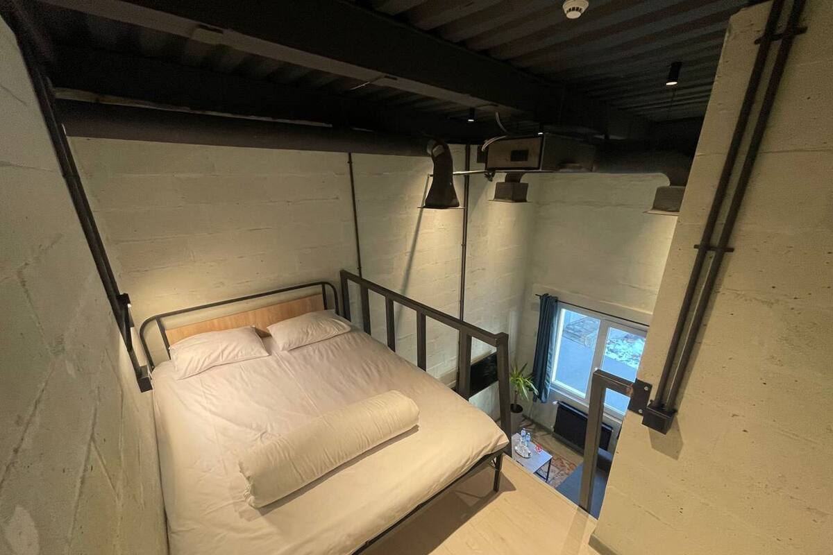 A bedroom with a bed, a window, and a small table with a plant.