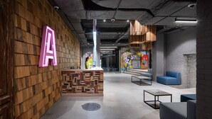 A modern reception area with a wooden wall and a large 'A' sign, a counter with a patterned design, and seating areas with blue sofas. - Campus Community A-Hotel (Kyiv)