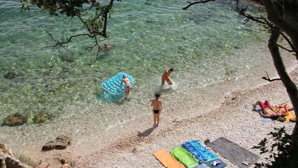 A beach scene with clear water, people swimming, and beach equipment.