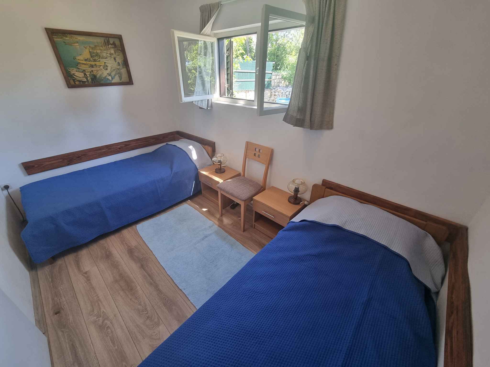 Een kamer met twee eenpersoonsbedden, een houten vloer, een klein tafeltje met een stoel, een raam met gordijnen en een schilderij aan de muur.