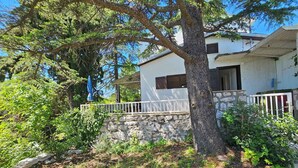 A house with a stone wall, a white balcony, and a large tree in front.