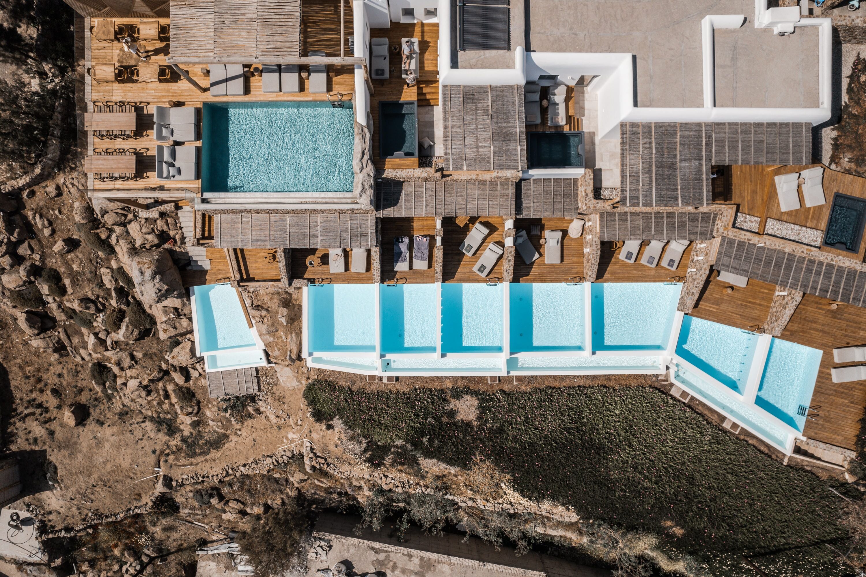 An aerial view of a resort with multiple swimming pools, sun loungers, and a rocky shoreline.