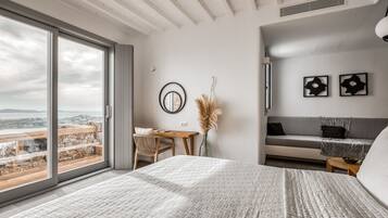 A modern bedroom with a large bed, a desk, and a sofa. There is a view of the city through large windows.