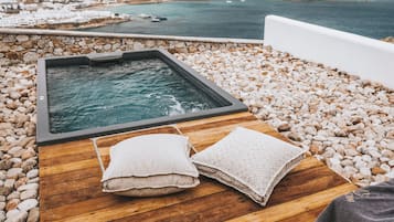 Une terrasse en bois avec un jacuzzi et des serviettes, donnant sur une zone côtière avec des bâtiments et des bateaux.