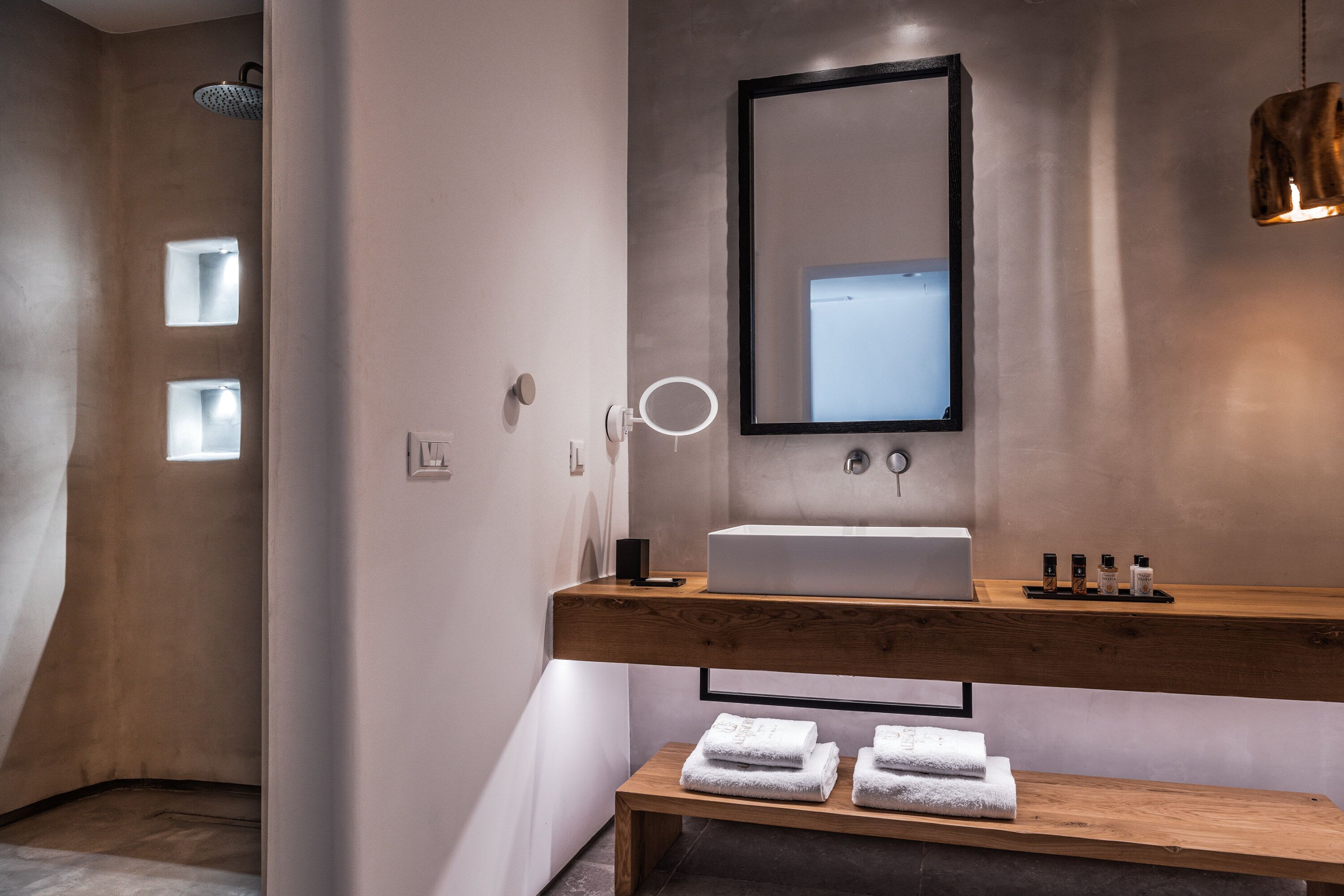 Une salle de bain moderne avec un meuble-lavabo en bois, un grand miroir et un banc avec des serviettes.
