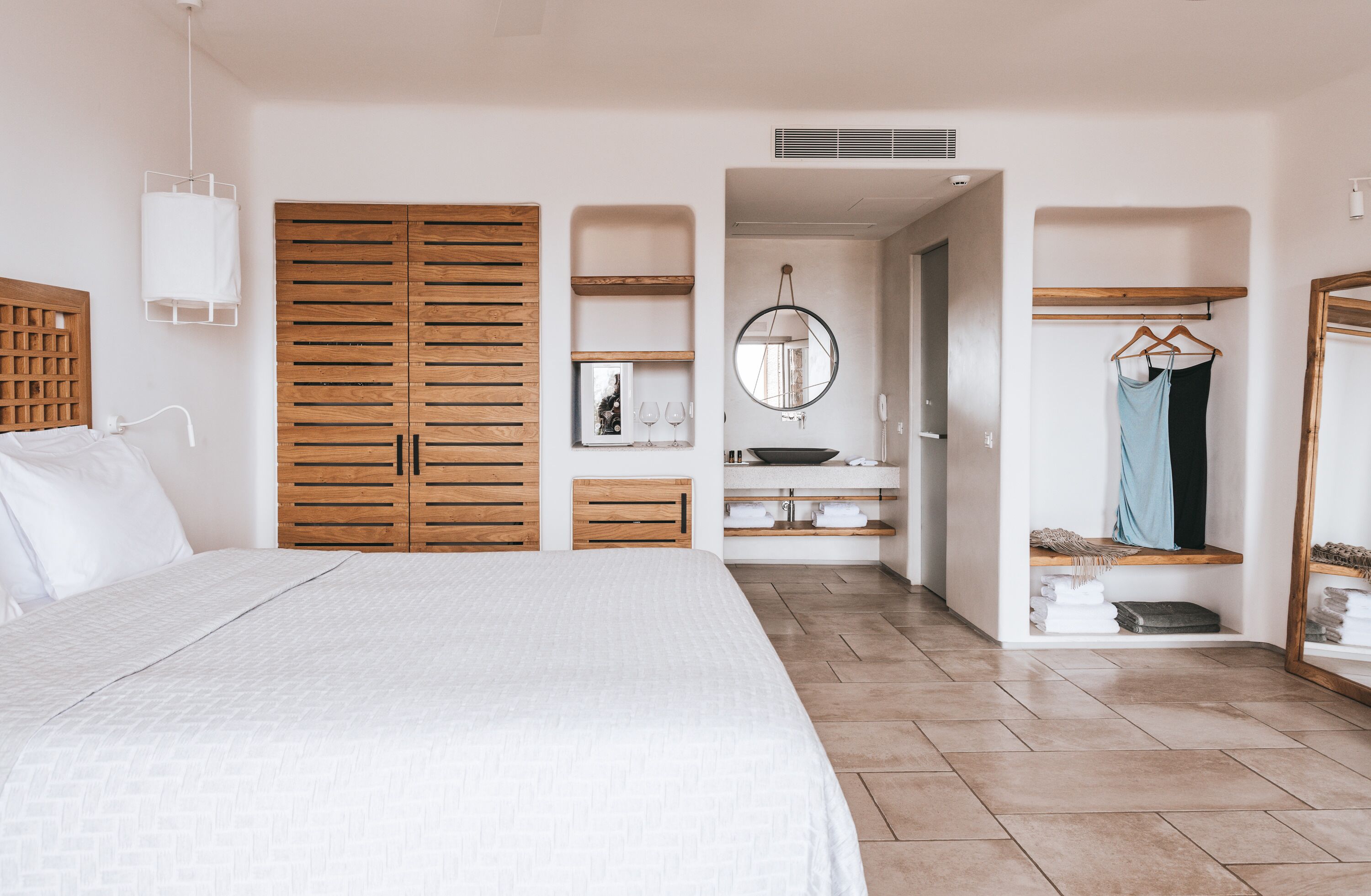 A bedroom with a large bed, wooden wardrobe, built-in shelves, a mirror, and a hanging light fixture.