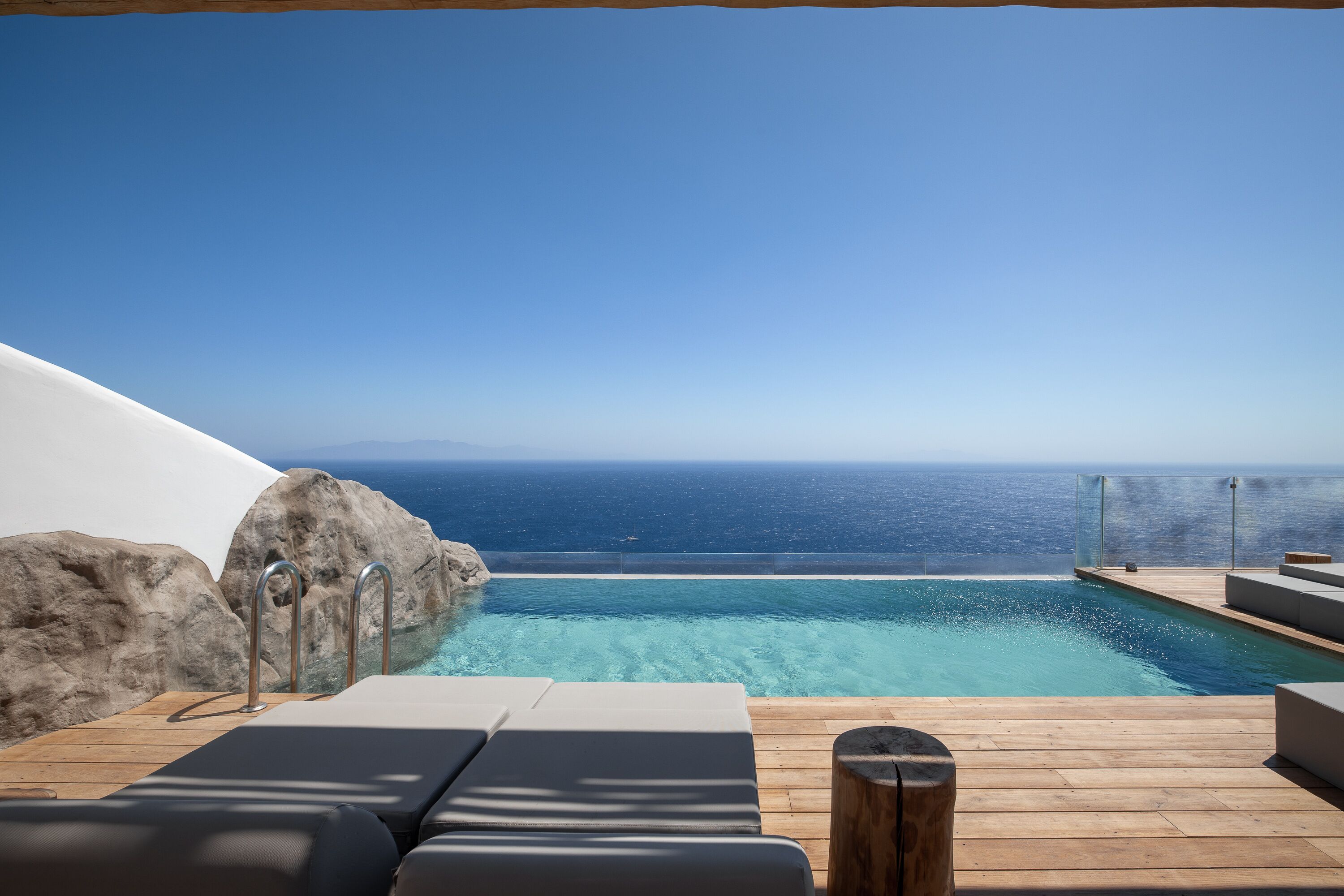 A poolside area with a view of the ocean, wooden deck, and lounge chairs.