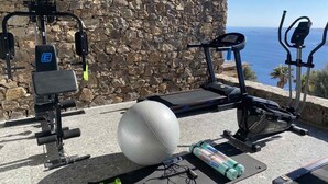 An outdoor gym with exercise equipment, a large exercise ball, and a yoga mat against a stone wall with a view of the sea. - Alissachni Mykonos (Mykonos)