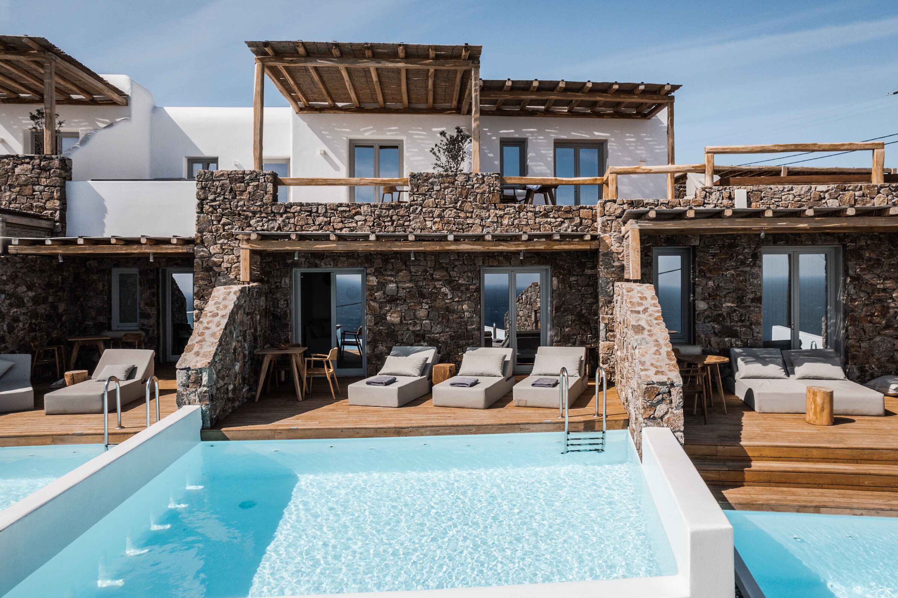 A poolside area with lounge chairs and a hot tub, stone walls, and wooden deck.