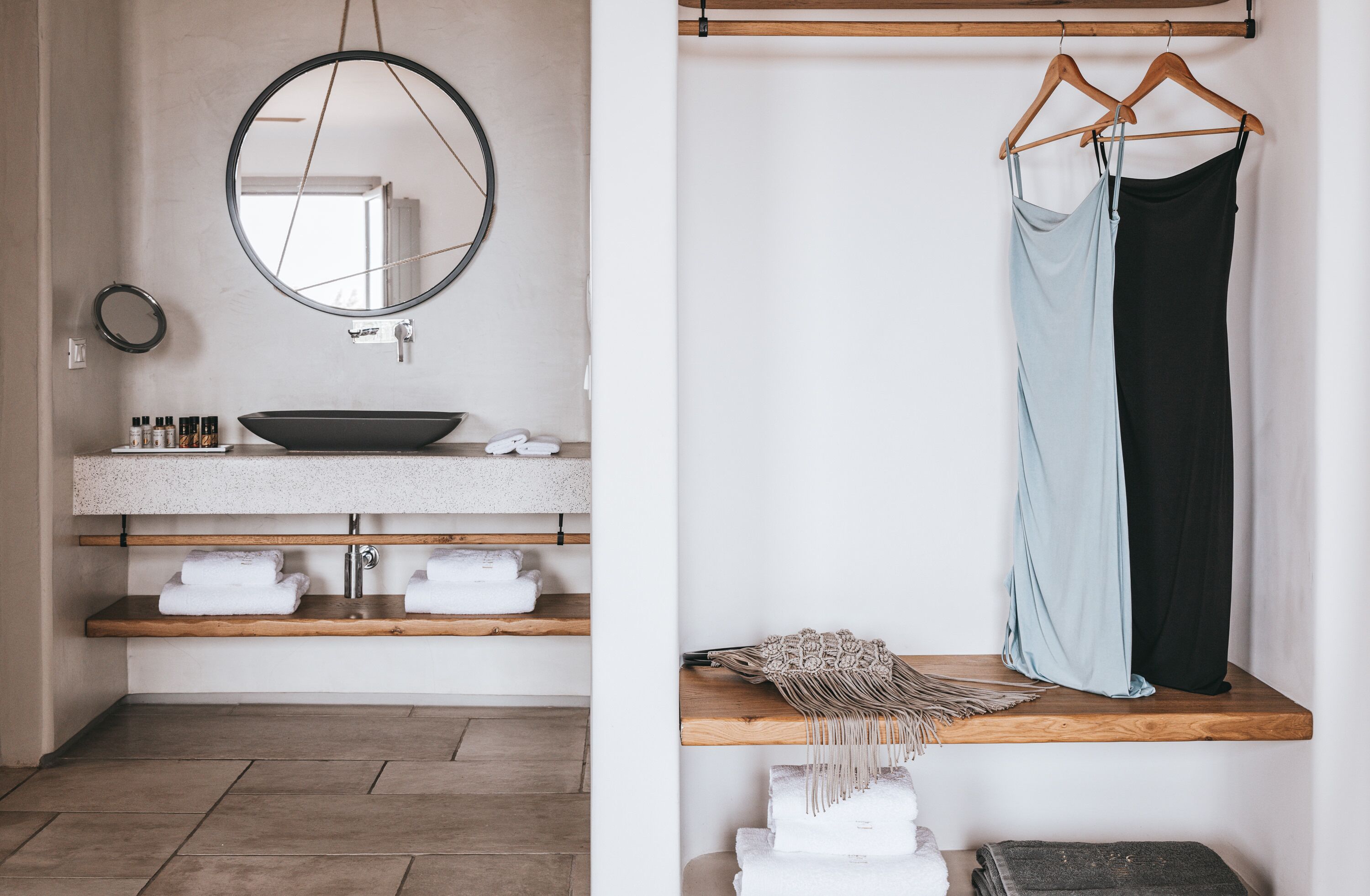 A bathroom with a round mirror, a sink with a bowl, and wooden shelves with towels.