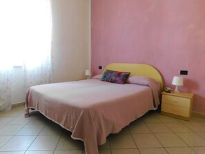 A bedroom with a bed, a nightstand, a lamp, and a wall clock. - Albergo Locanda Maria (Ameglia)