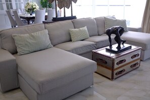 A modern living room with a beige sectional sofa, patterned pillows, and a decorative sculpture on a vintage-style chest.
