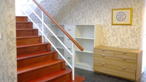 Een trap met een houten leuning, een houten dressoir en een wand met bloemenbehang.