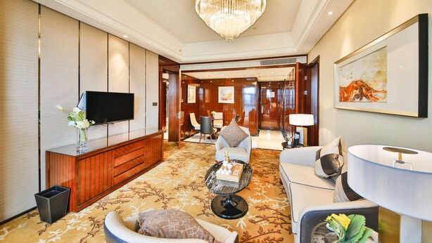 Un hall d’hôtel moderne avec un grand lustre, un téléviseur à écran plat, une console en bois, un canapé, une table basse et une œuvre d’art encadrée accrochée au mur.