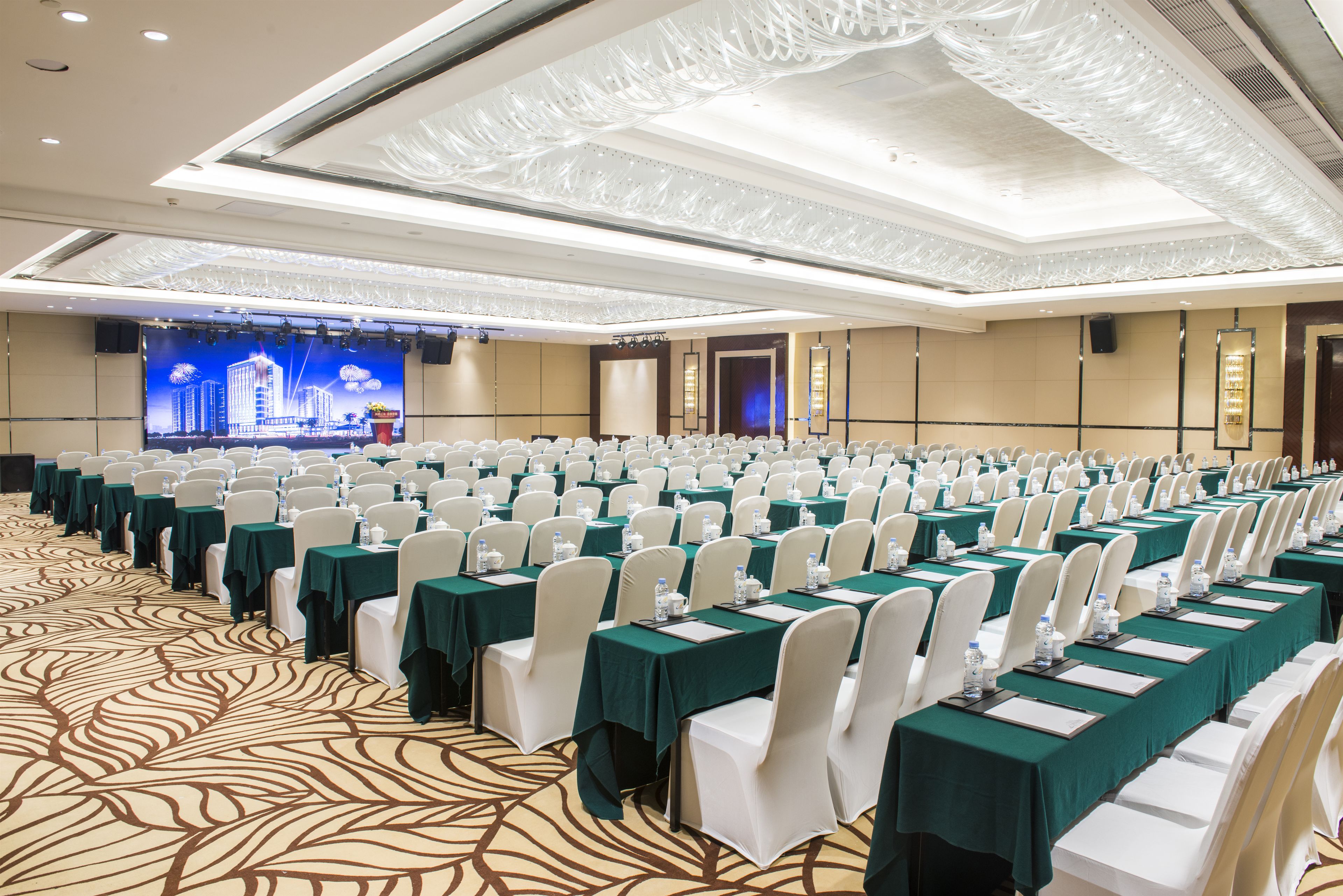 Un salón de conferencias con mesas dispuestas en filas, sillas blancas y un escenario con fondo azul.