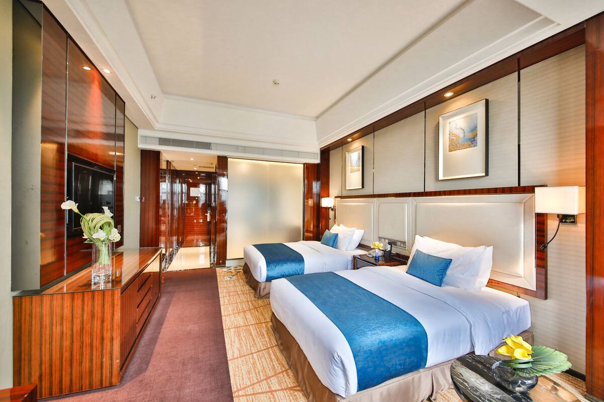 Habitación de hotel con dos camas, un mostrador de recepción de madera, un espejo grande y una obra de arte enmarcada en la pared.