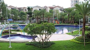 Un espace autour d’une piscine agrémenté d’un petit arbre, de pelouse et d’une fontaine.