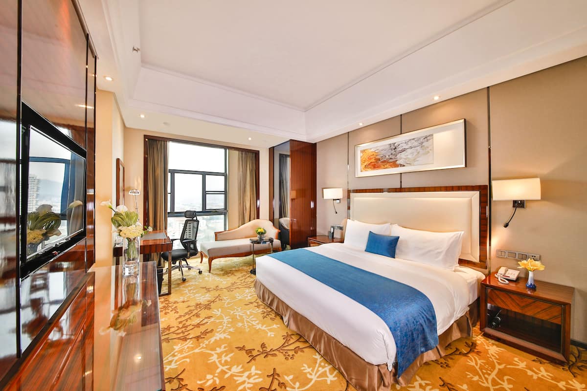 Una habitación de hotel con una cama grande, un escritorio, una silla, un televisor y una ventana con cortinas.
