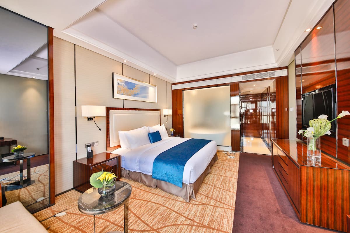 Una habitación de hotel moderna con una cama grande, un escritorio, una silla, una mesita con un florero y un espejo amplio.