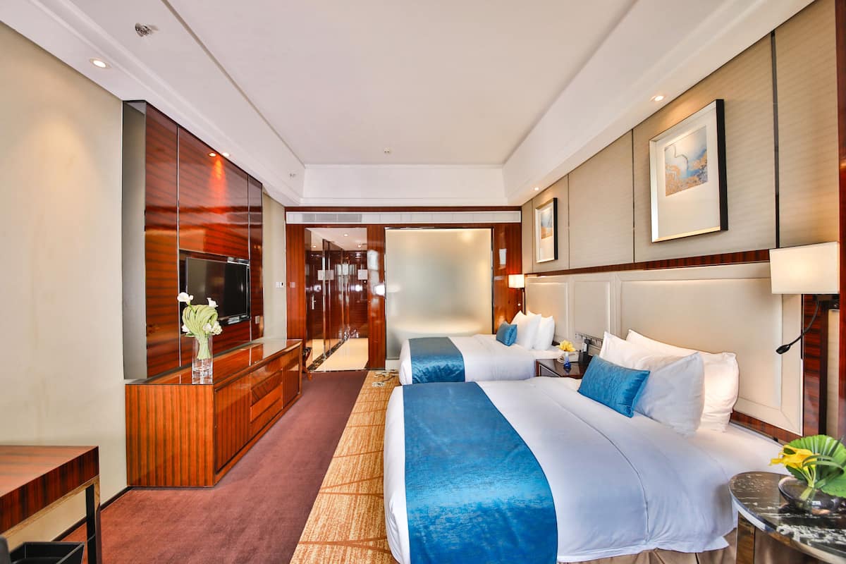 Habitación de hotel con una cama grande, un escritorio, televisión y baño visible a través de una puerta abierta.