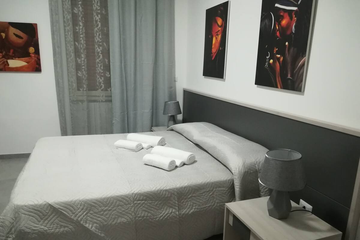 A neatly made bed with rolled towels, a bedside lamp, and artwork on the wall.