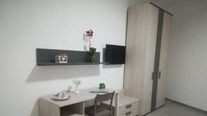 A modern bedroom with a wooden desk, a chair, a TV mounted on the wall, and a wardrobe.