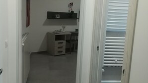 A narrow hallway with a door on the right leading to a room with a radiator and a small table with a plant.