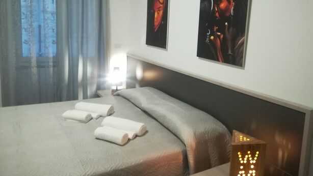 A hotel room with a bed, two wall-mounted artworks, a bedside lamp, and a night light.
