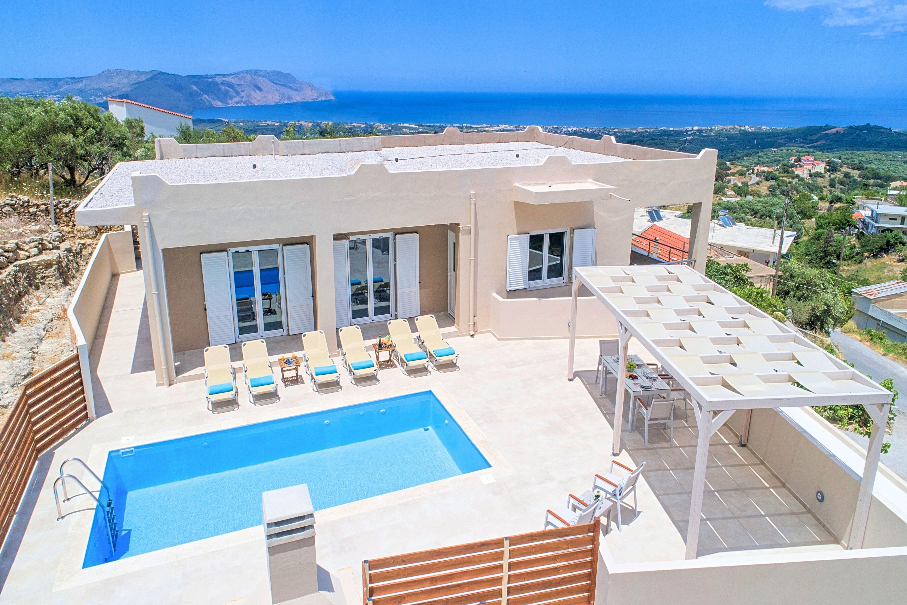 Une villa moderne dotée d’une piscine sur le toit, de chaises longues et offrant une vue sur la mer.