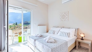 A hotel room with a bed, a bedside table with a lamp, a radiator, and a view of mountains through a sliding glass door. - Villa di Giorgio Heated Pool (Apokoronas)