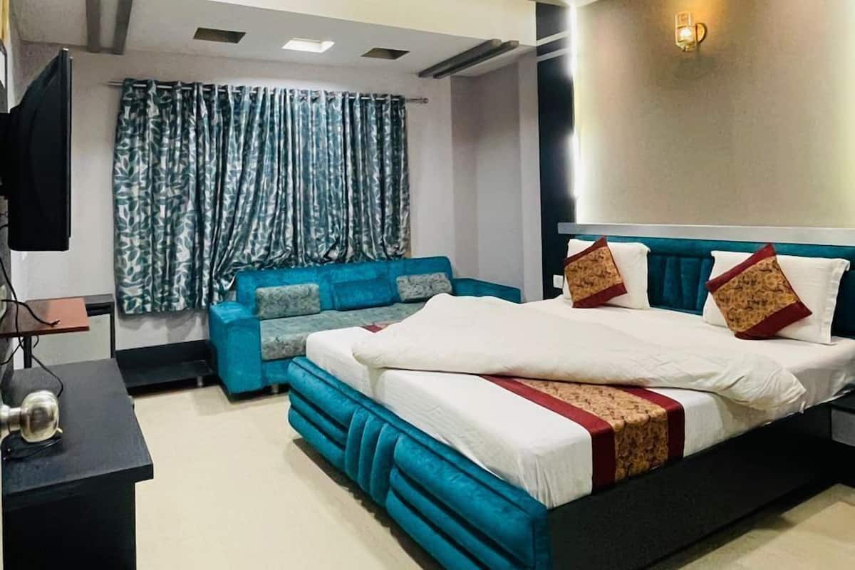 A modern bedroom with a large bed, a blue sofa, a TV, and a ceiling fan.