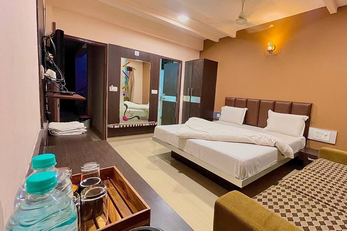 A hotel room with a bed, a desk with a chair, a wardrobe, and a mirror.