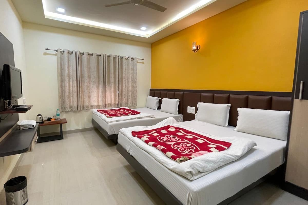 A hotel room with two beds, a TV, a small table with a kettle, and a window with curtains.