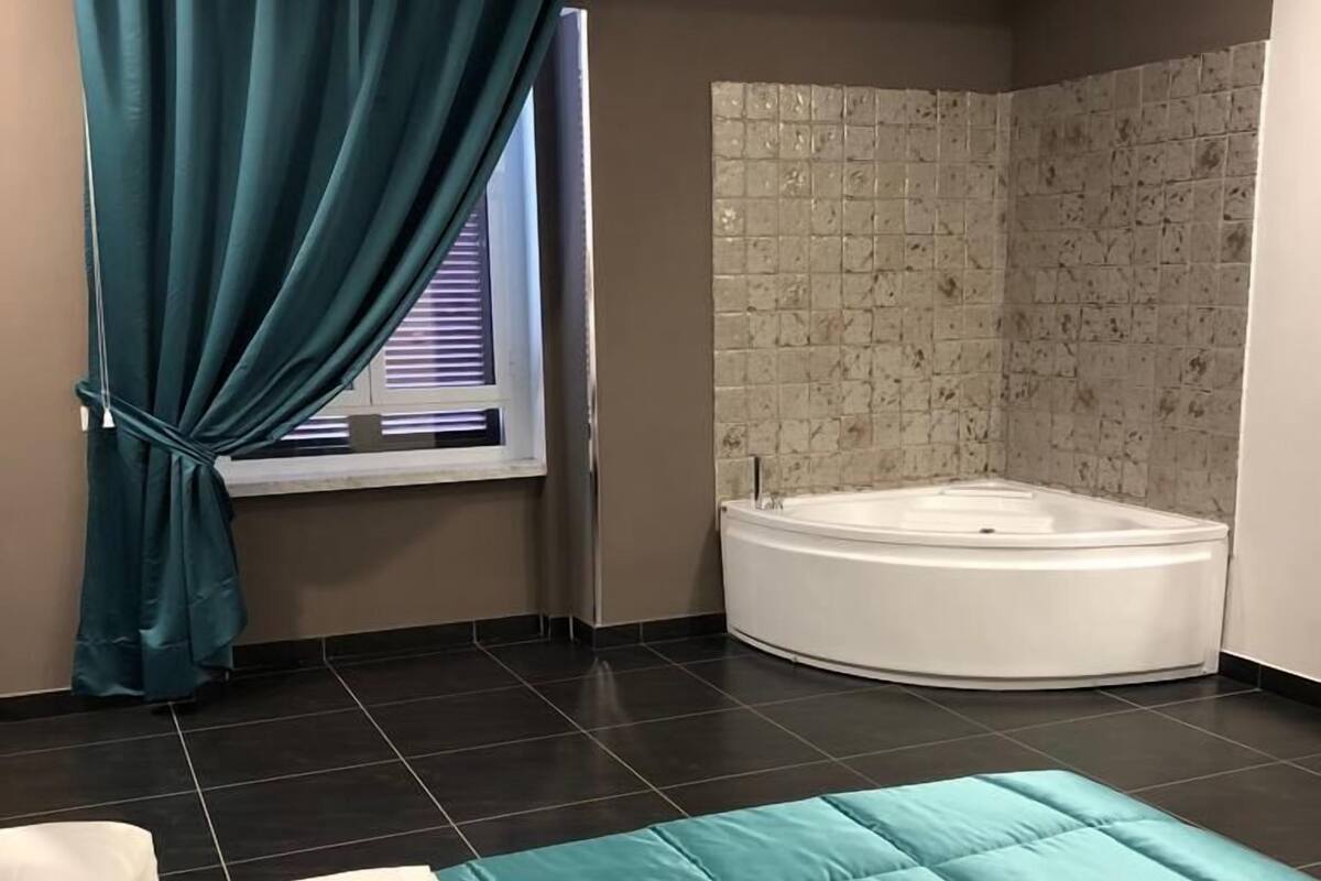 Un baño moderno con bañera, una ventana con cortinas y pared de ducha con azulejos.