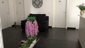 Ein modernes Wohnzimmer mit einer schwarzen Couch, einer dekorativen Uhr an der Wand und einer Reihe von Topfpflanzen.