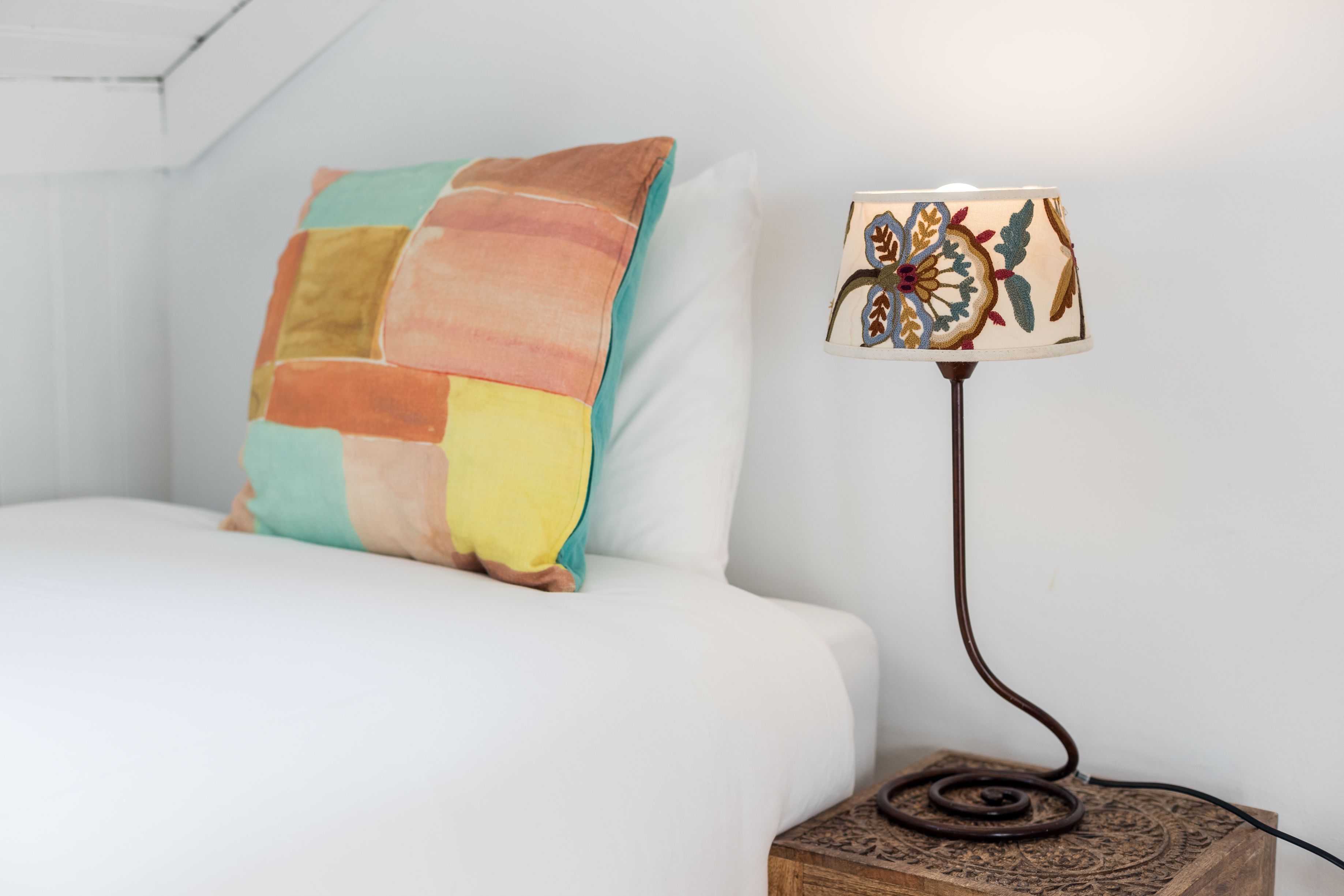 A bed with a colorful quilt and a lamp with a floral design on a wooden base.