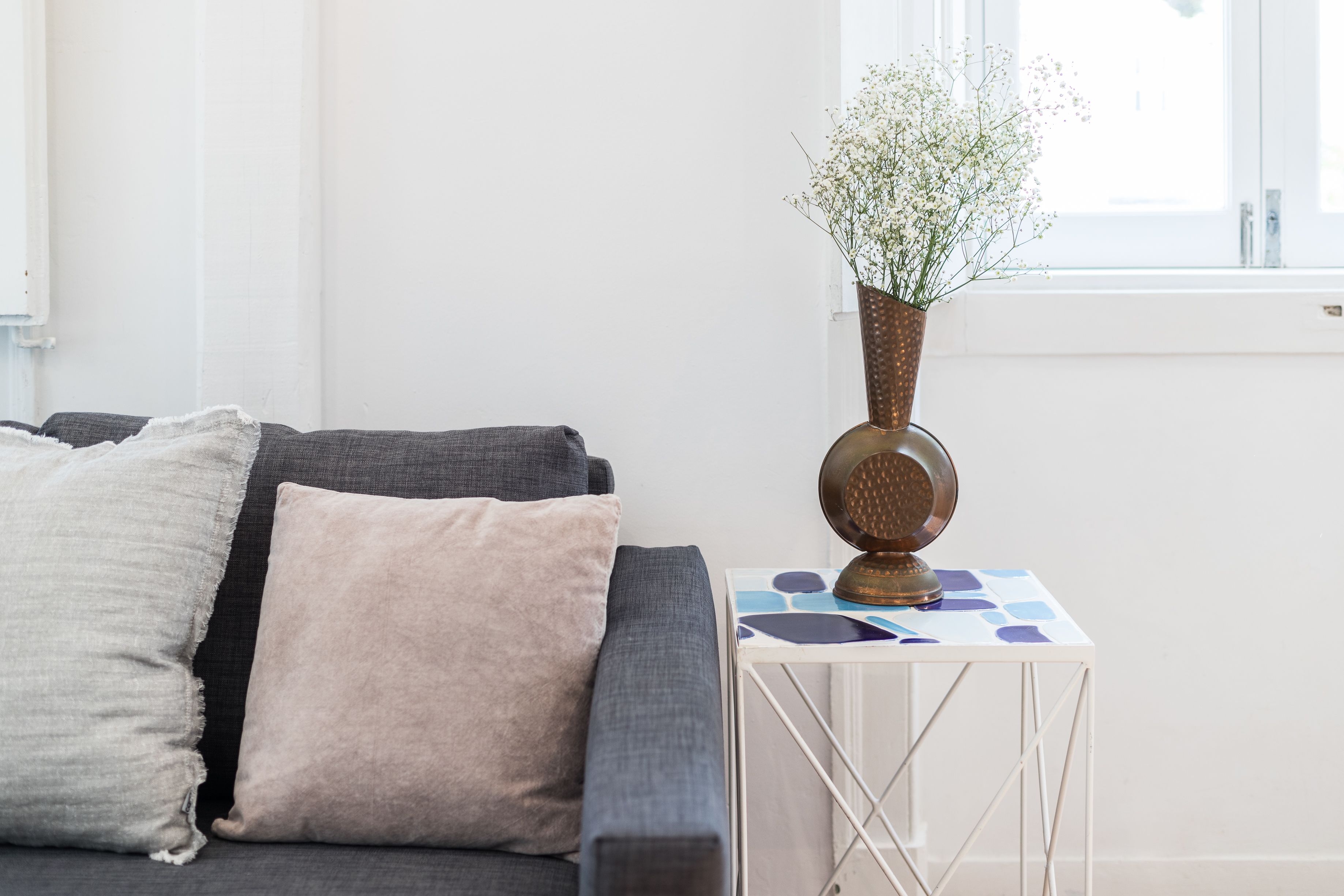 A modern living room with a grey sofa, a small white side table, and a vase with white flowers.