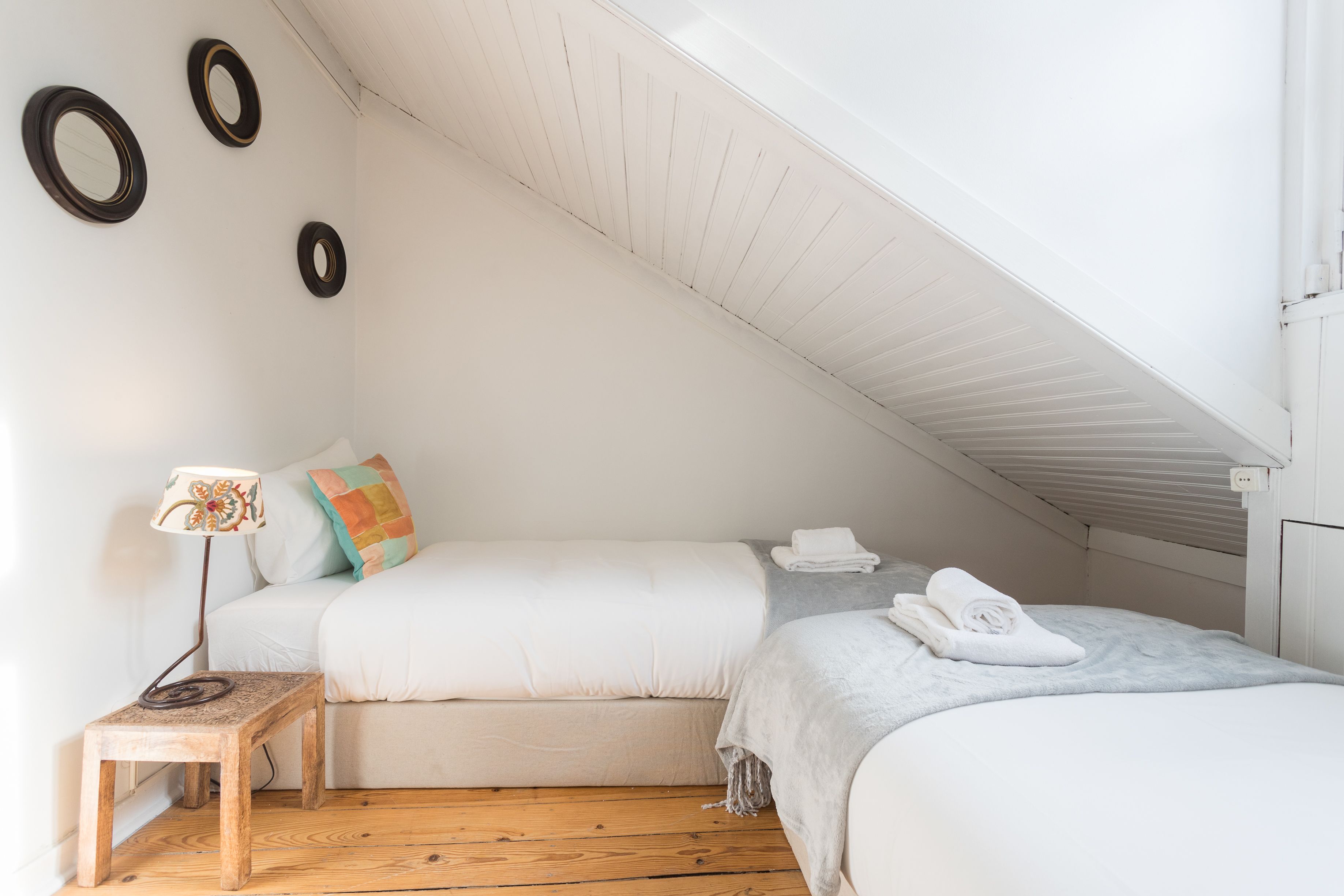 Een gezellig slaapkamer op zolder met schuine wanden, twee bedden, een klein houten tafeltje en een vloerlamp.