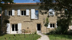 A stone building with a garden path leading to a door, a small table and chairs outside, and a stone fountain in the center.