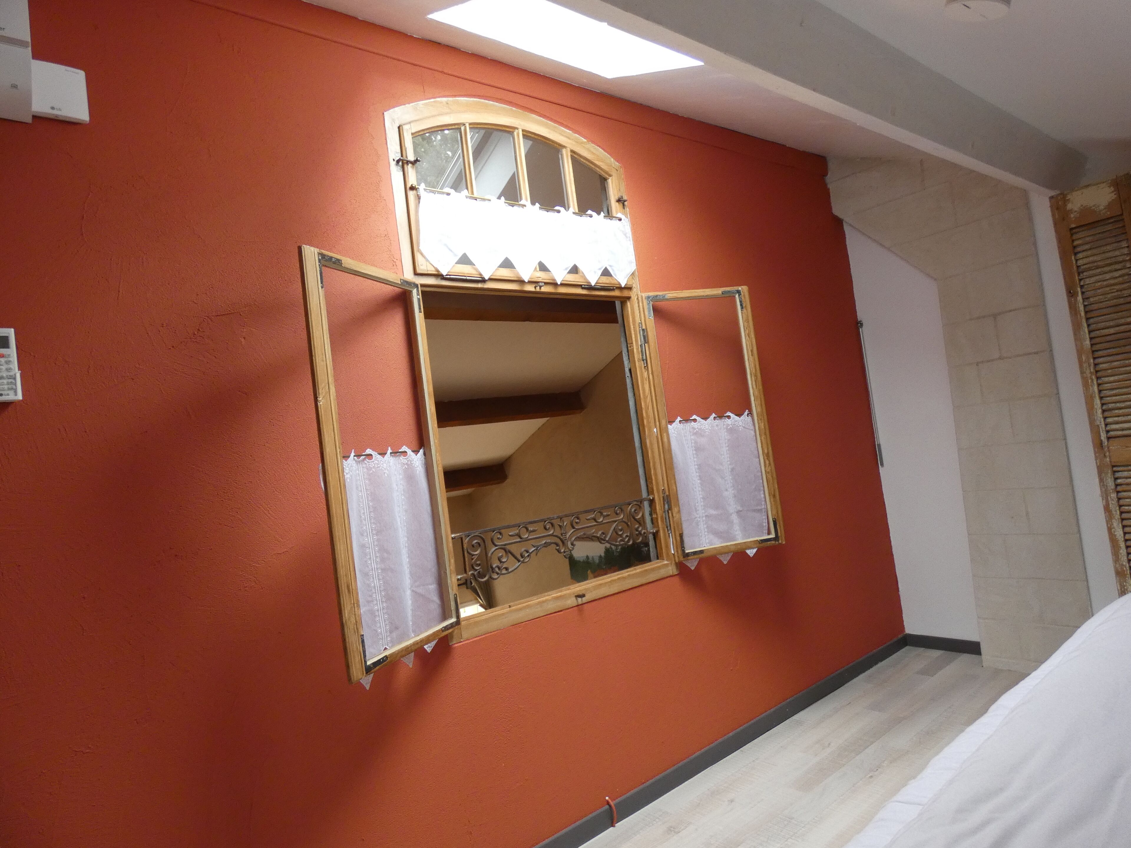 A room with a red wall, a wooden-framed mirror, and a white curtain.