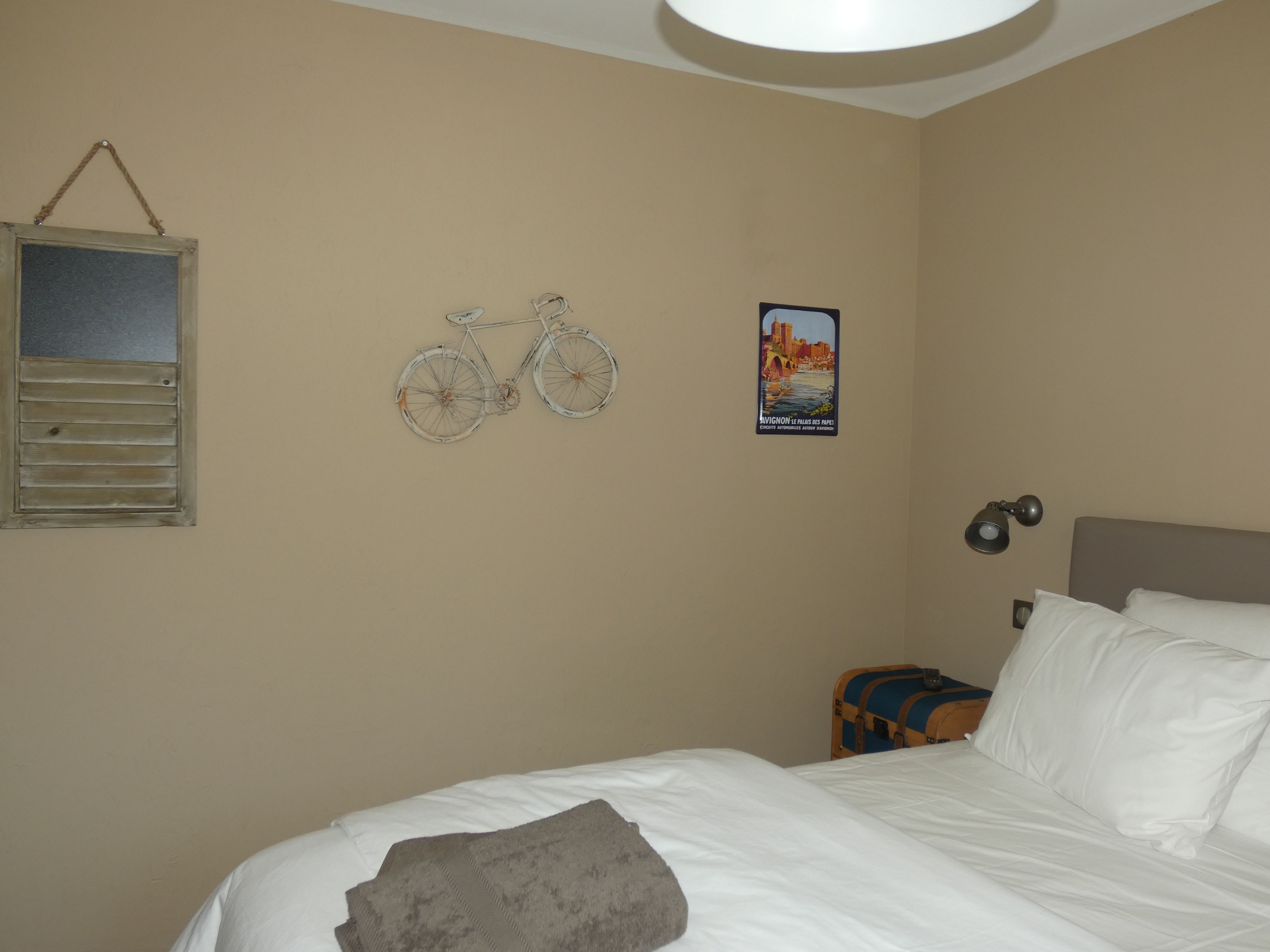 A bedroom with a bed, a wall-mounted bicycle, a poster, a lamp, and a suitcase.