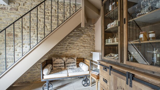 A staircase with a stone wall, a wooden bench with pillows, and a cabinet with jars.