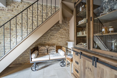 A staircase with a stone wall, a wooden bench with pillows, and a cabinet with jars.