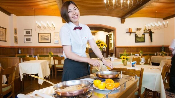 A restaurant with wooden interiors, tables set with white tablecloths, and a person serving food. - Zum Roten Bären (Freiburg im Breisgau)