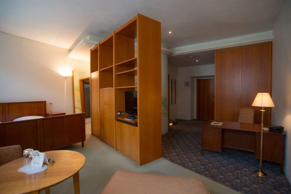 Una habitació d'hotel amb llit, escriptori, cadira, taula petita, armari i làmpada.