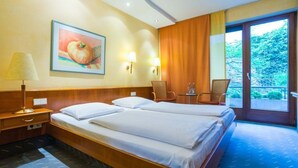 A hotel room with a double bed, two bedside tables, a lamp, a chair, a small table, and a painting on the wall. - Zum Roten Bären (Freiburg im Breisgau)