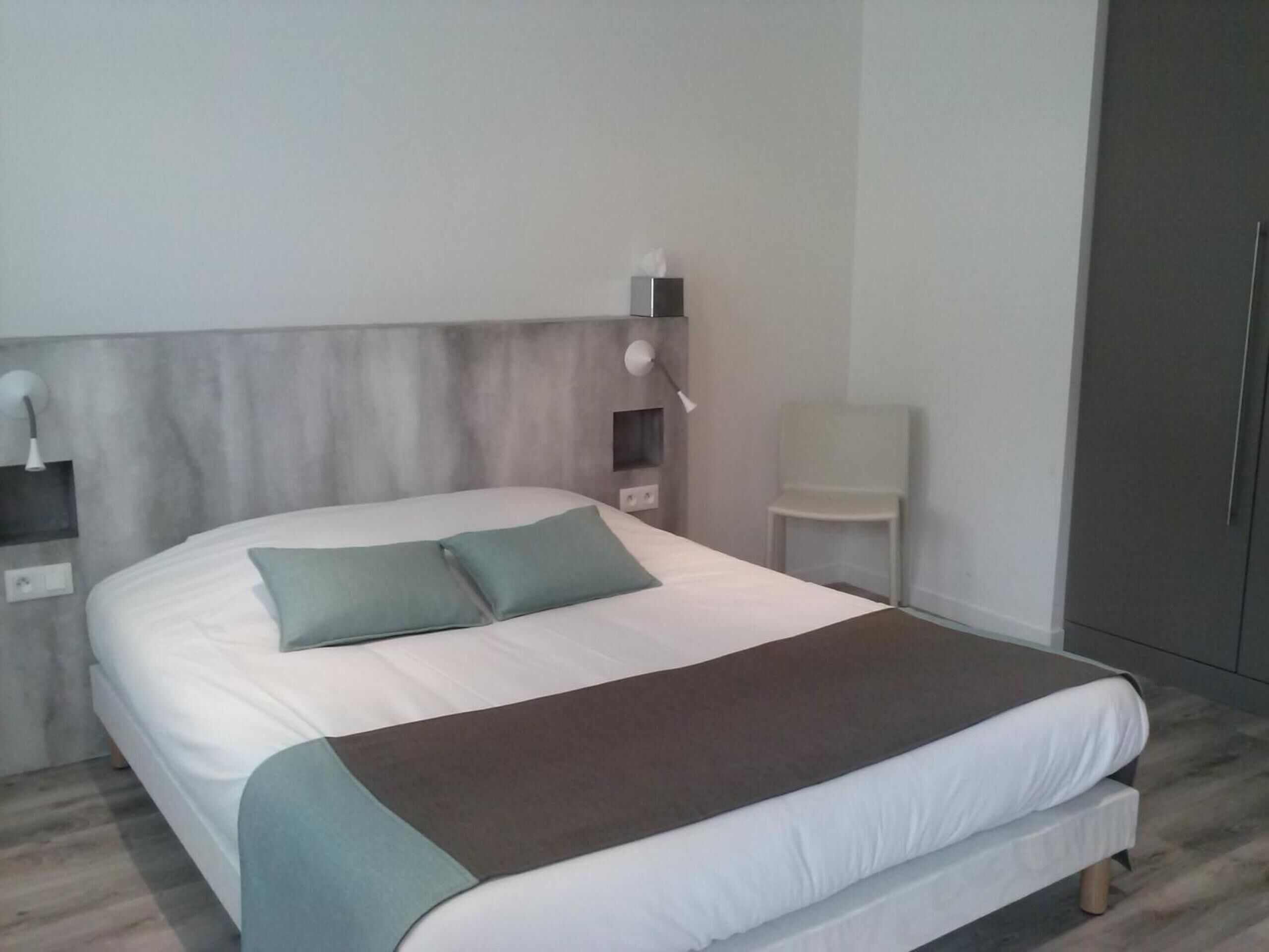 Un dormitorio moderno con una cama grande, una mesita de noche, una silla y un armario.