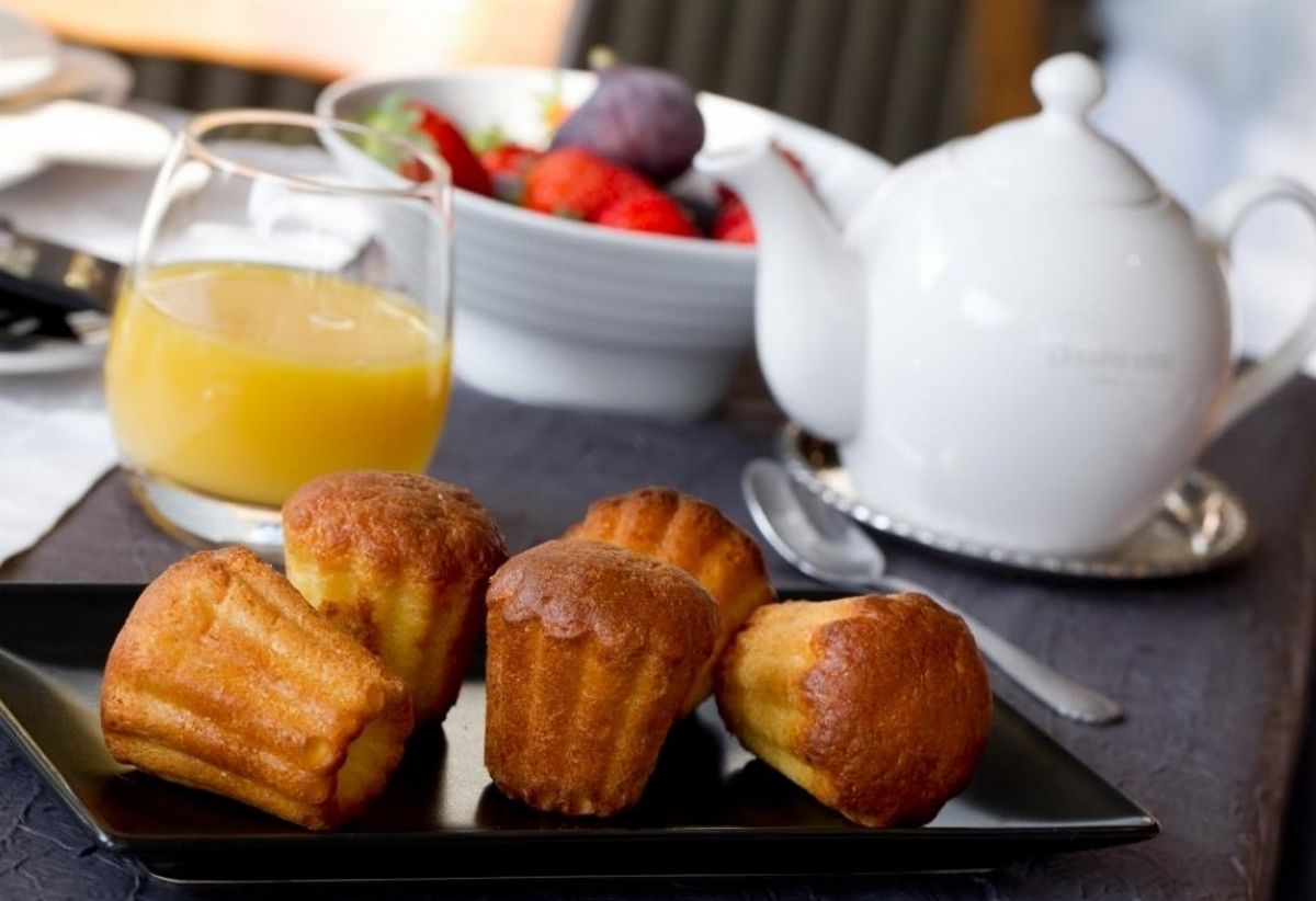 Une table dressée pour le petit-déjeuner, avec des viennoiseries, un verre de jus d’orange et une théière.
