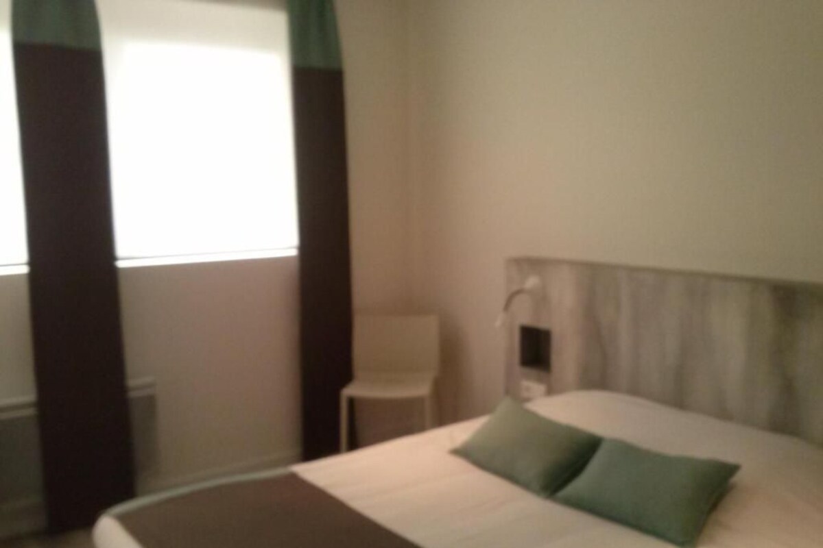Een hotelkamer met een bed, een stoel en een raam met gordijnen.
